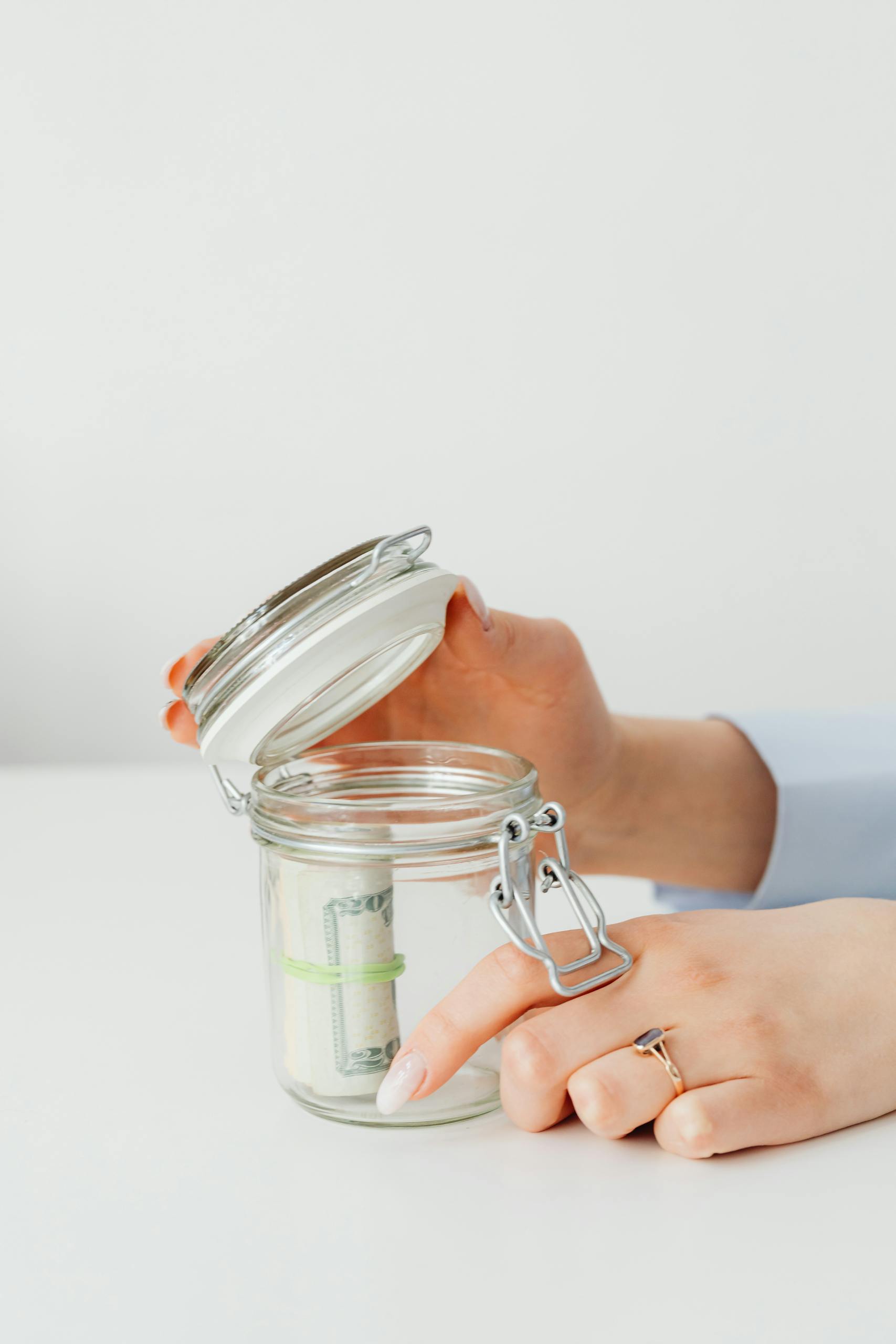 Close-up of hands placing money into a jar, symbolizing savings and financial planning.