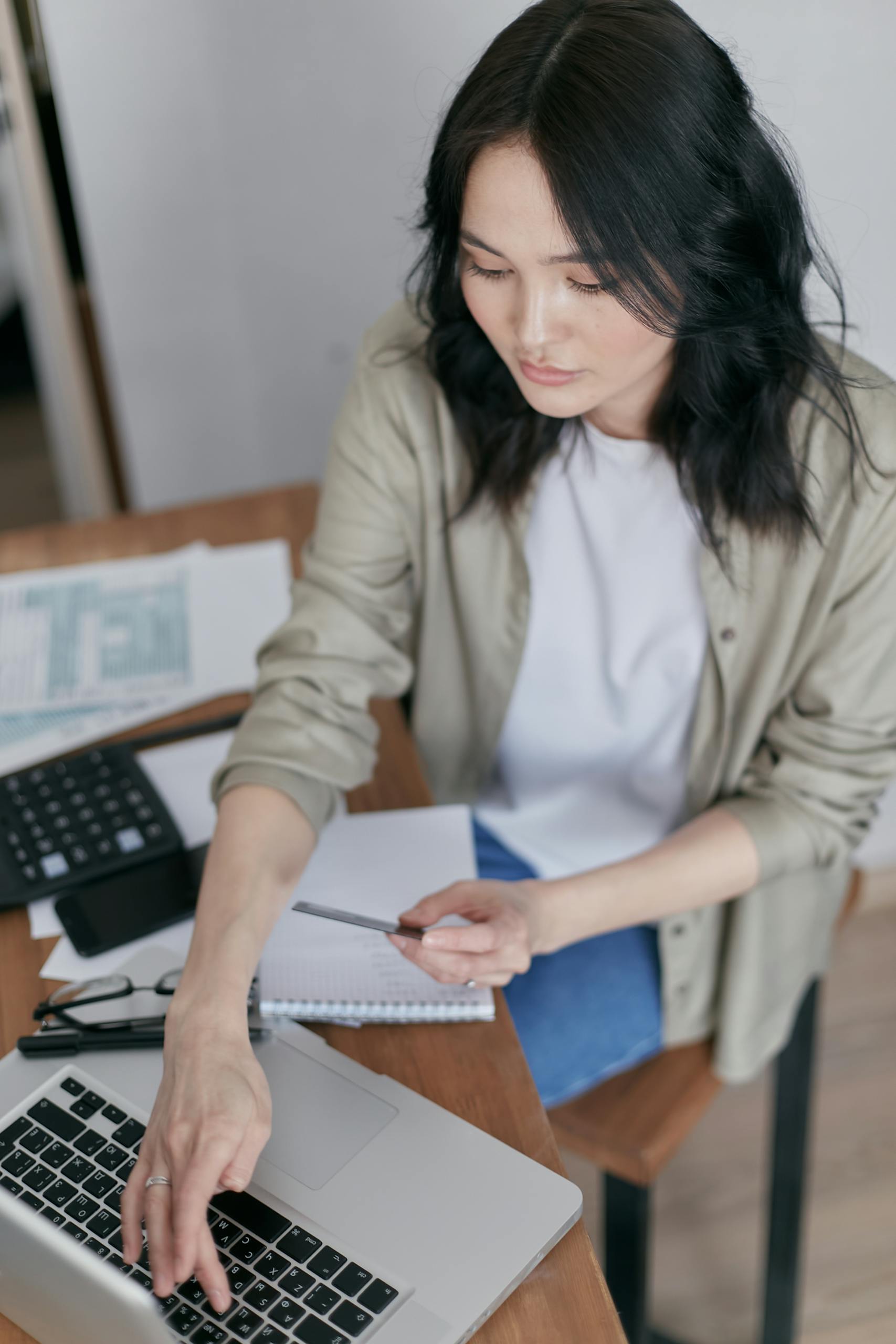 Focused woman working on a laptop at a wooden desk with office supplies.